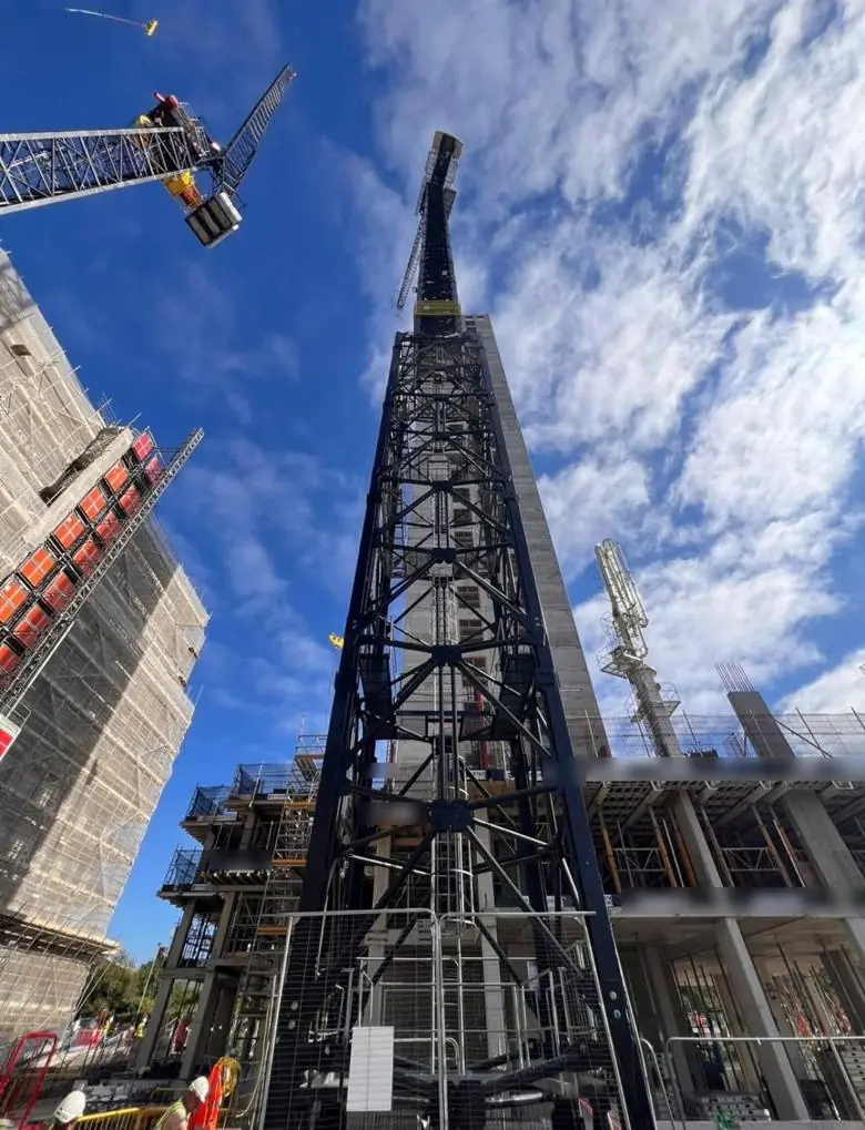 Looking up a tall tower crane mast beside a concrete frame under construction