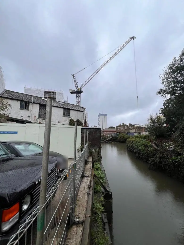 Luffing-jib tower crane working over a river next to a live site