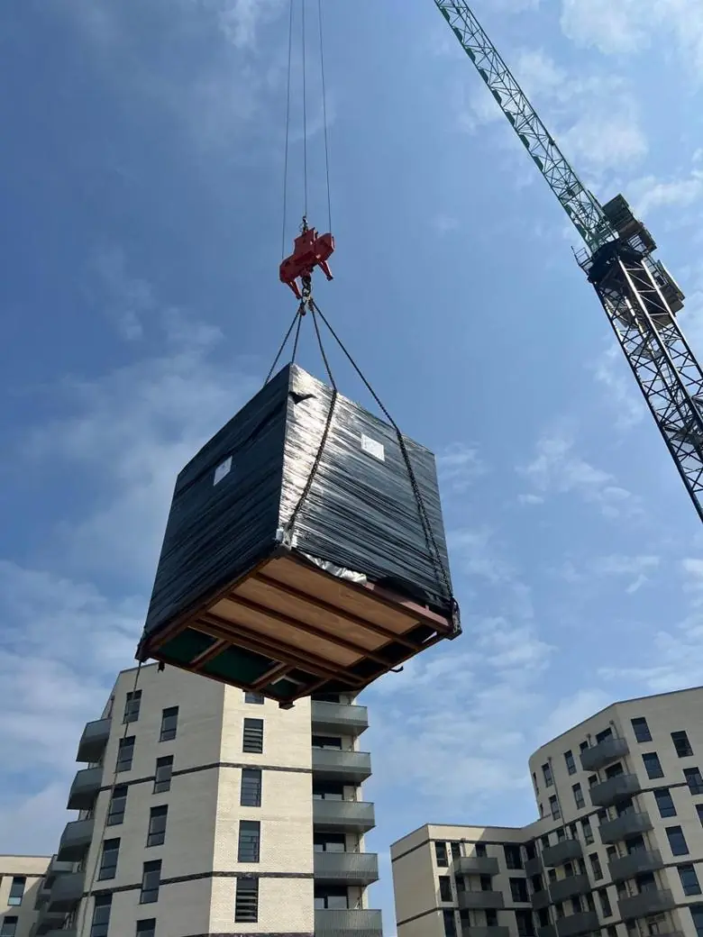 Tower crane lifting a wrapped pod on a four-leg chain sling