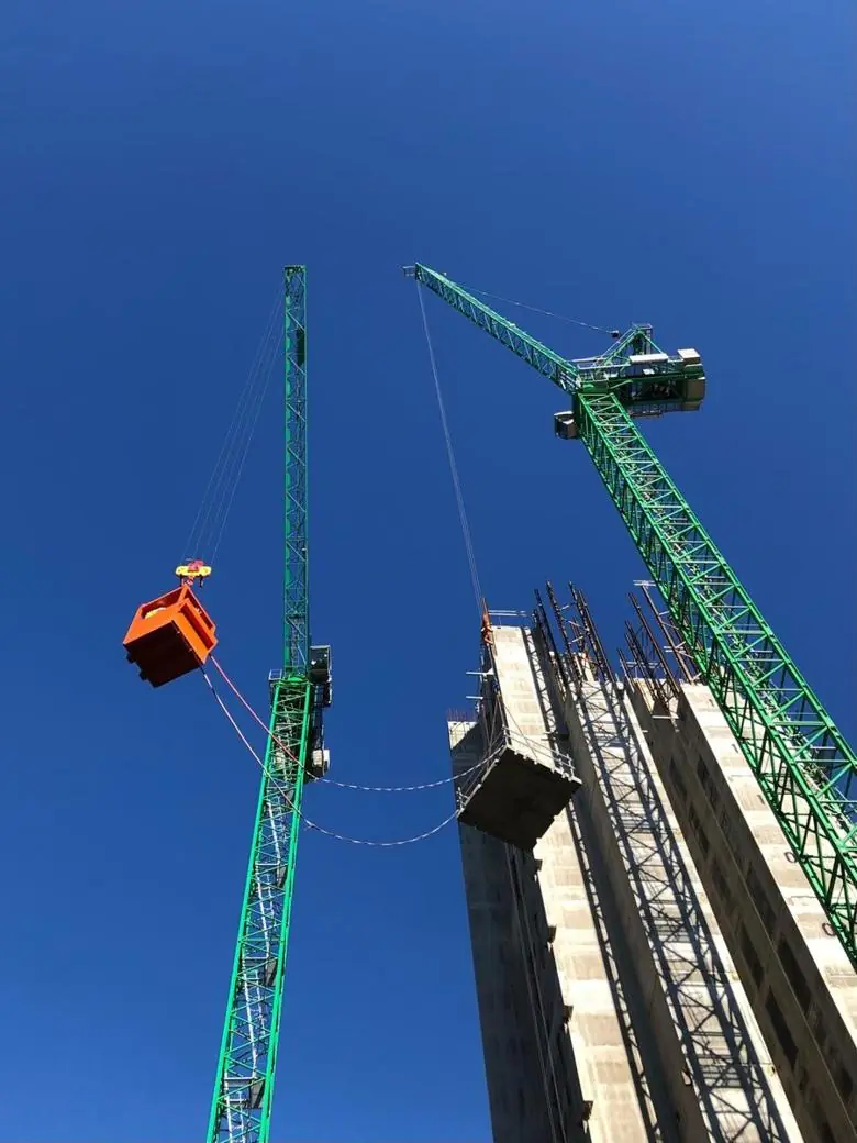 Green tower crane lifting a crane skip beside a high-rise concrete core
